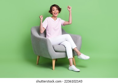 Photo of positive pretty lady wear trendy stylish outfit sit comfy chair raise arm hand rejoice enjoy isolated on green color background