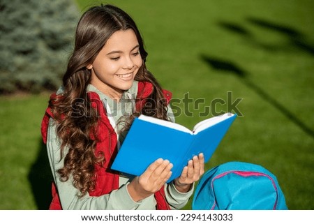photo of positive school teen girl read in park. school teen girl read outdoor.