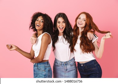 Photo of a positive smiling pleased young three multiethnic girls friends posing isolated over pink wall background.
