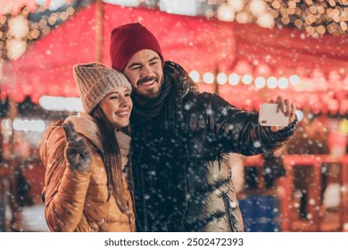 Photo of positive two people couple students take selfie smartphone girl make v-sign in x-mas christmas noel city fair evening illumination lights around outdoors outside - Powered by Shutterstock