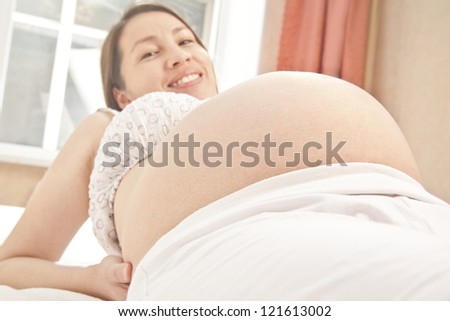 Photo of pregnant woman lying and looking at camera  on window curtains background