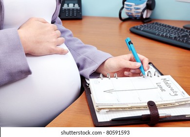 Photo Of A Pregnant Woman In An Office Writing The Words Maternity Leave In Her Diary.