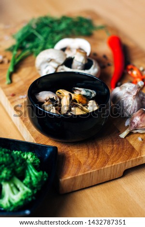 Photo of a preparation of ingridients such as musseles, red chilli peppers, fresh greens, mushrooms, broccoli with attractive woman hands on a wooden table