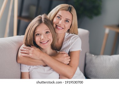 Foto de la adorable hija de una madre que viste camisetas blancas sonriendo sofás cubiertos en el interior de la habitación Foto de stock