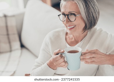 Photo of pretty adorable elderly lady wear white cardigan drinking coffee watching television indoors apartment room - Powered by Shutterstock