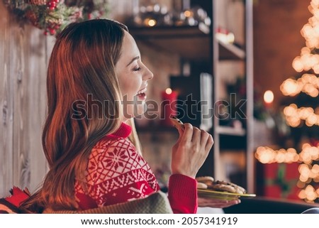 Photo of pretty adorable mature lady wear red pullover smiling eating christmas chocolate cookies indoors house home room