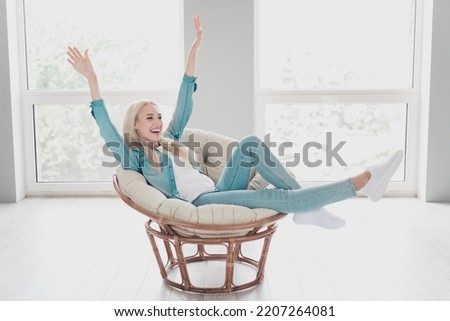 Photo of pretty adorable young lady dressed denim shirt relaxing armchair rising hands arms indoors apartment