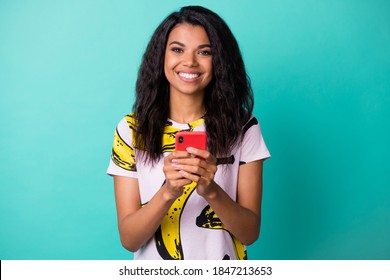 Photo Of Pretty Black Lady Hold Smartphone Shiny Smile Look Camera Wear Banana Print T-shirt Isolated Teal Color Background