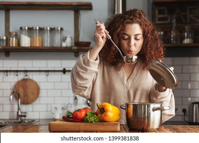 Photo of pretty caucasian woman holding cooking ladle spoon while eating soup with fresh vegetables in kitchen at home