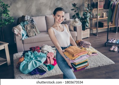 Photo of pretty charming lady stay home quarantine sorting tidy clean clothes hold hands stack wardrobe stuff donating old belongings poor people volunteer living room indoors