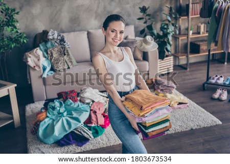 Photo of pretty charming lady stay home quarantine sorting tidy clean clothes hold hands stack wardrobe stuff donating old belongings poor people volunteer living room indoors