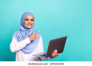 Photo of pretty charming young woman wear arab headscarf writing modern gadget pointing empty space isolated turquoise color background