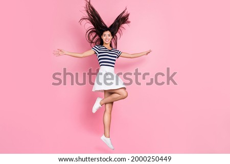 Photo of pretty charming young woman wear striped outfit jumping high empty space smiling isolated pink color background