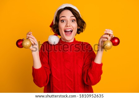 Photo of pretty cheerful funny excited lady celebrate winter holidays hold christmas balls present decorate green tree wear santa cap red knitted sweater isolated yellow color background