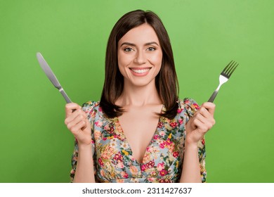 Photo of pretty cheerful girl beaming smile arms hold knife fork isolated on green color background