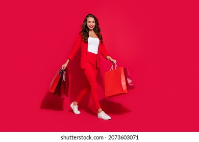 Photo of pretty classy young lady dressed suit blazer walking holding shopping bags empty space smiling isolated red color background - Powered by Shutterstock