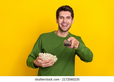 Photo of pretty cute guy dressed green pullover eating popcorn changing channels isolated yellow color background - Powered by Shutterstock