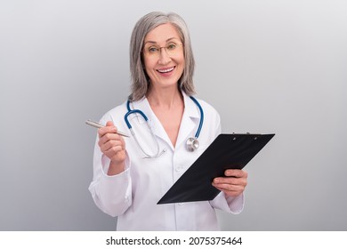 Photo Of Pretty Cute Senior Woman Doc Dressed White Uniform Glasses Writing Clipboard Smiling Isolated Grey Color Background