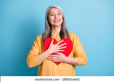 Photo of pretty dreamy old lady white grey hairstyle hands hold embrace paper red heart figure imagine youth love self concept wear yellow sweater isolated blue pastel color background