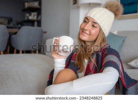 Photo of pretty dreamy young woman dressed winter hat sitting couch cover blanket drinking coffee indoors house home room