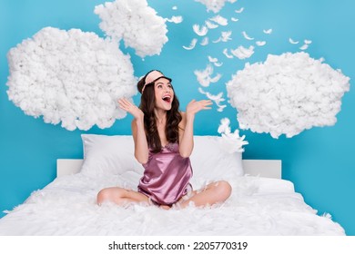 Photo of pretty excited lady wear pink pajama sitting bed flying white feather empty space isolated blue color background - Shutterstock ID 2205770319
