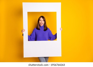 Photo of pretty funny lady dressed violet sweater holding paper photo frame winking tongue isolated yellow color background