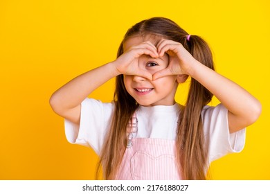 Photo Of Pretty Funny School Girl Wear Summer Overall Arms Showing Heart Cover Eye Isolated Yellow Color Background