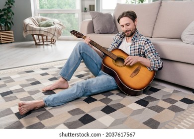 Photo of pretty handsome young man wear plaid shirt smiling sitting floor playing guitar indoors house room - Powered by Shutterstock