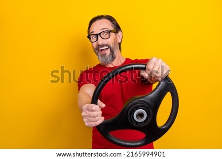 Photo of pretty impressed retired man wear red t-shirt spectacles riding car smiling isolated yellow color background