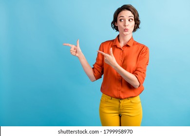 Photo of pretty shocked lady direct fingers side look interested empty space demonstrate presenting low prices poster wear orange office shirt yellow trousers isolated blue color background