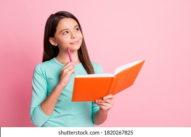 Photo of pretty sweet little clever thoughtful latin girl long hairdo arms hold orange diary pen cheekbone look up empty space wear turquoise sweatshirt isolated pink color background