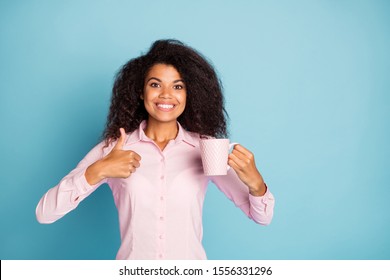 Photo Of Pretty Wavy Dark Skin Lady Holding Hot Beverage Mug Raising Thumb Up Advising Colleagues Try Fresh Coffee Wear Pink Shirt Isolated Blue Color Background