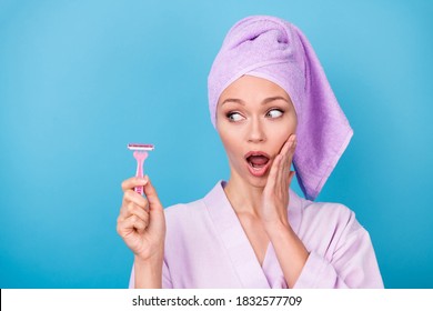 Photo of pretty woman look side hold pink razor arm cheekbone open mouth wear purple towel turban bathrobe isolated blue color background