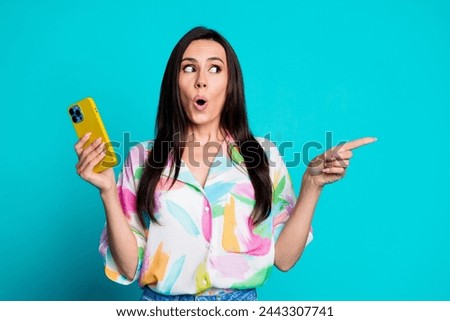 Photo of pretty young woman hold smart phone point finger empty space wear shirt isolated on teal color background
