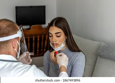 Photo of a professional lab technician in a face shield inserting the swab into the young female patient throat at home.Close up of a young woman having a nasal swab test done by her doctor.Copy space