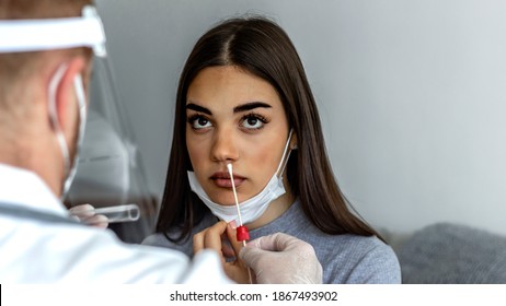 Photo of a professional lab technician in a face shield inserting the swab into the young female patient throat at home.Close up of a young woman having a nasal swab test done by her doctor.Copy space