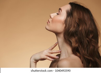 Photo in profile of half naked pretty woman 20s with long auburn hair touching her neck with closed eyes isolated over beige background