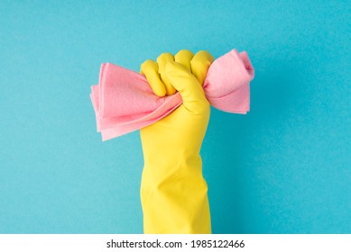Photo of raised hand in yellow glove clenching pink rag into fist on isolated blue background with copyspace