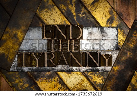Photo of real authentic typeset letters forming End The Tyranny text on vintage textured grunge silver gold and copper layered background