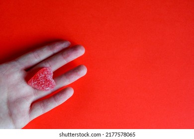 Photo Of Red Jelly Candy Heart In Hand Of Woman On Red Background