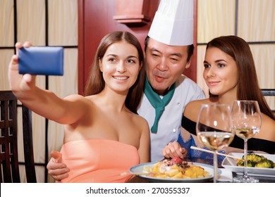 Photo to remember. Two beautiful smiling women doing selfie with a Japanese chef-cook in a restaurant - Powered by Shutterstock