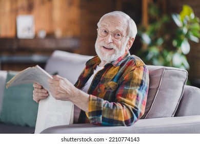 Photo of retired old man grandpa grey hair hold newspaper have break smile wear casual checkered clothes specs sit sofa indoors home room