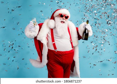 Photo of retired old man grey beard carefree hold bottle glass sparkling wine midnight club celebration confetti wear santa x-mas costume suspender sunglass cap isolated blue color background