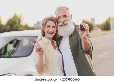 Photo of retired pensioner grey haired wife husband old people new car keys v-sign cool outside outdoors in city