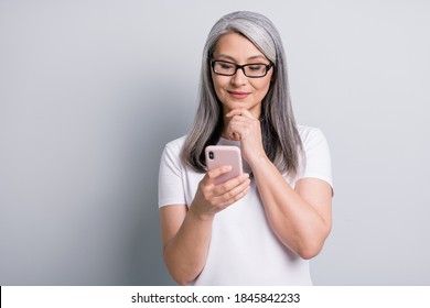 Photo of retired woman hold cellphone finger chin look screen wear spectacles white t-shirt isolated grey color background