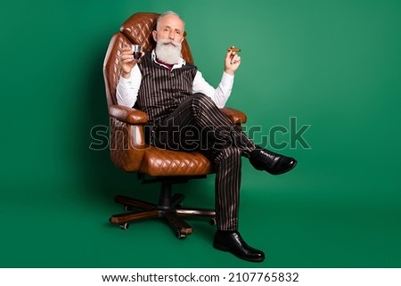 Photo of rich english gentleman sit chair drink whiskey smoke cigar wear striped suit on green color background