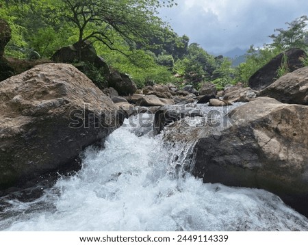a photo of a river with lots of rocks and clear water flowing fast. The river is located on the slopes of Mount Muria, Indonesia