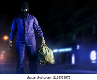 Photo Of Robber In Mask, Overalls, Gloves, Bag And Gun Standing Front View On Night Street Background.