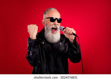 Photo rockstar singer man hold mic sing retro hit song wear sunglass leather jacket isolated red color background