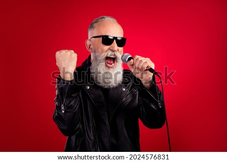 Photo of rockstar singer man hold mic sing retro hit song wear sunglass leather jacket isolated on red color background